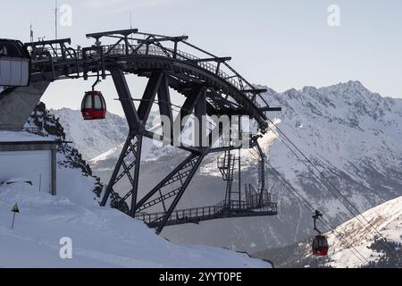 Passo Tonale, Italia - 28.01.2023: Funivie rosse che si spostano lungo una struttura in acciaio sopra il paesaggio innevato delle montagne, aspre cime sullo sfondo, Foto Stock