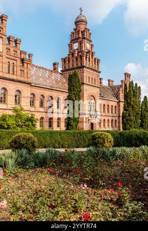 Un grande edificio in mattoni con una torre dell'orologio e un cortile con fiori. L'edificio è vecchio e ha molta storia Foto Stock