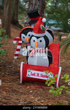 Due personaggi di pinguini giocattolo in una slitta vestita per Natale. Vestiti rossi e neri canna da zucchero e cappelli. Erba verde, foglie marroni e alberi nella schiena Foto Stock