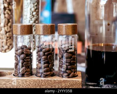 Primi piani di caffè in tre tubi di vetro vicino alla decorazione di bottiglie di vetro sul bancone del bar o sullo sfondo della caffetteria. Ingredienti per il makin Foto Stock