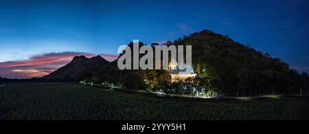 Una vista panoramica mozzafiato di una catena montuosa con campi colorati e case sparse sotto un vibrante cielo al tramonto. La scena cattura bea naturale Foto Stock