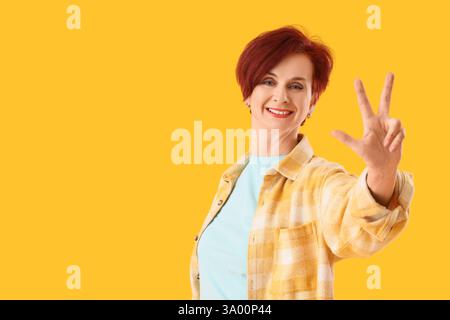 Donna matura che mostra tre dita su sfondo giallo. Concetto di regole Foto Stock