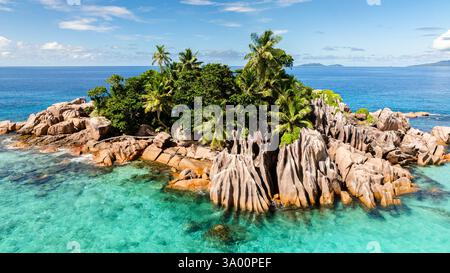Diverse barche ancorate da un'isola rocciosa e lussureggiante con vibranti acque turchesi e incontaminate barriere coralline. Isola di St Pierre. Seychelles. Foto Stock