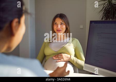 Sorridente donna incinta discutere con ginecologo femminile durante la visita in clinica medica all'ospedale Foto Stock