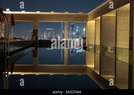 Lo skyline illuminato di Dubai si riflette in una piscina sul tetto di notte in inverno Foto Stock