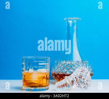 Un decanter di cristallo e un bicchiere basso che regge whisky sono disegnati su un vivace sfondo blu, che mostra lusso e semplicità nel design. Foto Stock