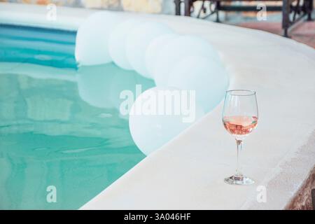 Bicchiere di vino rosa a bordo piscina con palloncini, dopo la festa Foto Stock