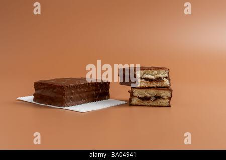 Una torta al cioccolato giace su carta bianca. Un'altra torta è tagliata a metà. Entrambe le torte sono su sfondo marrone. Foto Stock