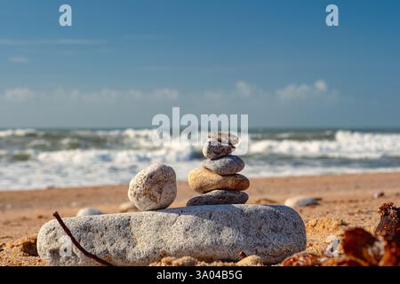Bellissima installazione di pietre marine sulla spiaggia. Una torre di ciottoli sorge su una grande pietra sullo sfondo dell'oceano. Cielo limpido, giorno di sole Foto Stock
