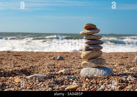 Bellissima installazione di pietre marine sulla spiaggia. Una torre di ciottoli sorge su una grande pietra sullo sfondo dell'oceano. Cielo limpido e grande W Foto Stock