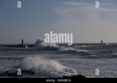 Un faro e un molo di cemento sulla riva di un oceano infuriante. Enormi onde si schiantano contro i muri, creando un effetto esplosivo. Schiuma bianca e spra Foto Stock