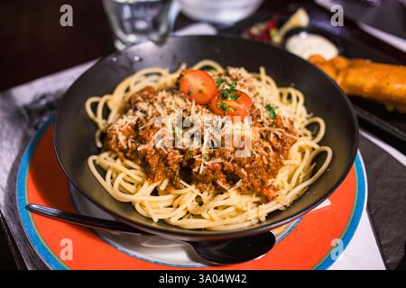 Spaghetti con salsa di manzo macinata e formaggio in piatto nero presso il ristorante italiano Foto Stock
