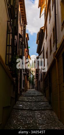Stretti gradini di pietra nel quartiere Albaicín di Granada arrampicati verso il patrimonio moresco e accoglienti balconi sotto il chiaro cielo pomeridiano andaluso Foto Stock