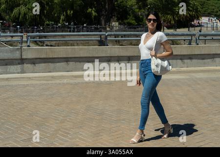 Giovane donna latina elegante che cammina con sicurezza sul marciapiede della città in una giornata di sole Foto Stock