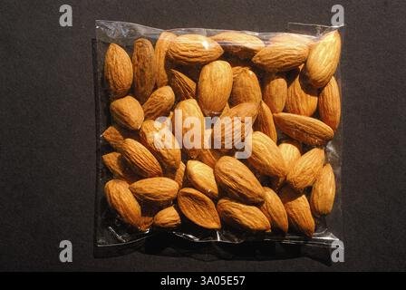 Frutta secca, mandorle confezionate in sacchetto di plastica trasparente per la vendita al dettaglio su sfondo nero Foto Stock