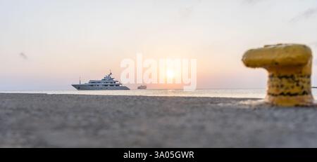 Barca di lusso ormeggiata al molo sulla costa di Kos con Blue Star Ferry sullo sfondo e dissuasore giallo in primo piano Foto Stock