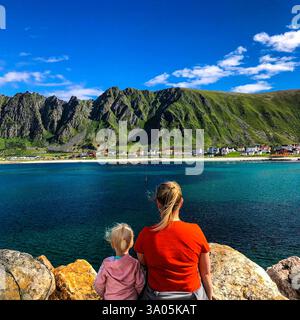 Una madre e una figlia stanno insieme sulle rocce, osservando le acque turchesi e le spettacolari montagne di Bleik, Andøya. Una famiglia perfetta. Foto Stock