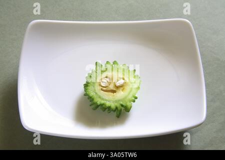 Verdure verdi, fetta di gourd amaro karela momordica charantia in piatto rettangolare su sfondo grigio Foto Stock
