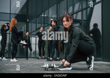 Lacci di lacci. Un gruppo di donne sportive si trova all'aperto vicino all'edificio nero. Foto Stock
