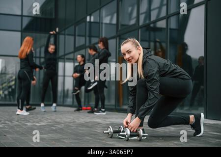 Lacci di lacci. Un gruppo di donne sportive si trova all'aperto vicino all'edificio nero. Foto Stock