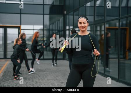 Con corda gialla. Un gruppo di donne sportive si trova all'aperto vicino all'edificio nero. Foto Stock