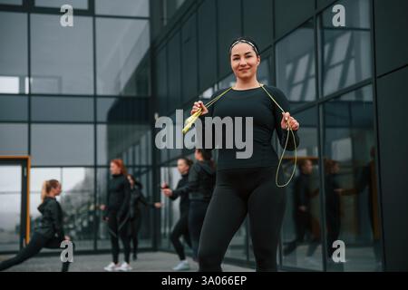 Con corda gialla. Un gruppo di donne sportive si trova all'aperto vicino all'edificio nero. Foto Stock