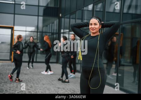 Con corda gialla. Un gruppo di donne sportive si trova all'aperto vicino all'edificio nero. Foto Stock