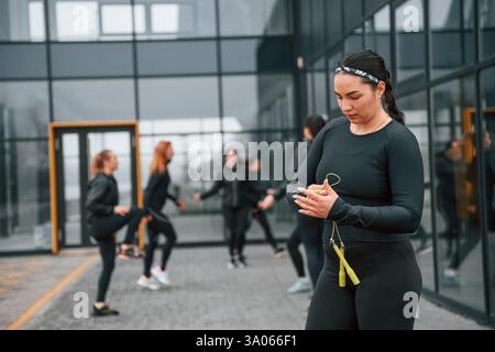 Con corda gialla. Un gruppo di donne sportive si trova all'aperto vicino all'edificio nero. Foto Stock