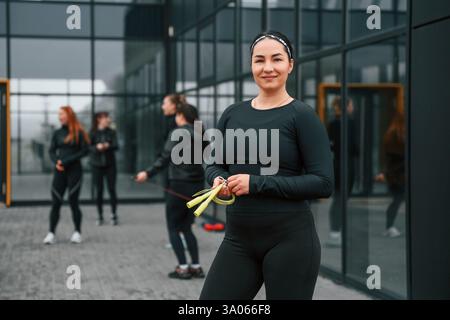 Con corda gialla. Un gruppo di donne sportive si trova all'aperto vicino all'edificio nero. Foto Stock