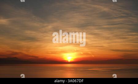 Tramonto dorato sul lago di Ginevra, che riflette una luce calda sull'acqua e sul cielo nuvoloso in Svizzera Foto Stock