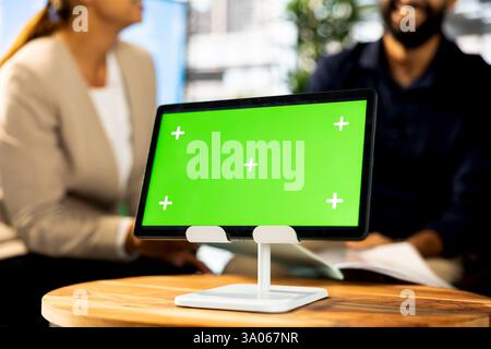 Concentratevi sul tablet con schermo verde utilizzato dal CEO in background sfocato durante l'incontro con i membri del Consiglio di amministrazione. Primo piano di un dispositivo di mockup in un moderno spazio di lavoro utilizzato dal personale Foto Stock