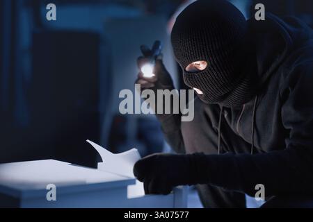 Ladro mascherato che tiene e legge documenti riservati Foto Stock