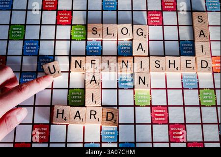 Un gioco Scrabble con una persona che crea la parola "incompiuto" Foto Stock