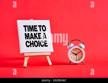 Tela bianca che mostra l'ora della frase per effettuare una scelta e una sveglia su sfondo rosso, il concetto di fare una scelta e il tempo sta per scadere Foto Stock