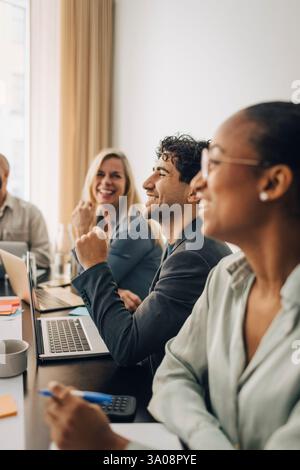Giovane uomo d'affari felice seduto con un computer portatile vicino a colleghi di sesso femminile nella sala riunioni dell'ufficio Foto Stock