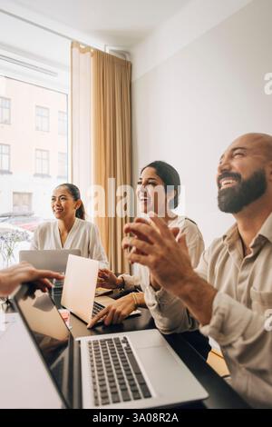 Professionisti creativi uomini e donne felici seduti con un computer portatile al tavolo nella sala riunioni dell'ufficio Foto Stock