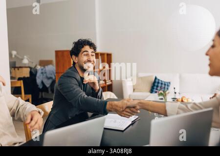 Un giovane uomo d'affari sorridente che stringe la mano con una collega nella sala riunioni dell'ufficio Foto Stock