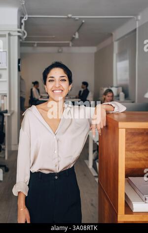 Ritratto di un'imprenditrice sorridente in piedi vicino alla scrivania in ufficio Foto Stock