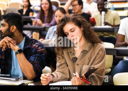 Giovane studentessa che legge un libro mentre siede da un amico maschio nella sala conferenze Foto Stock
