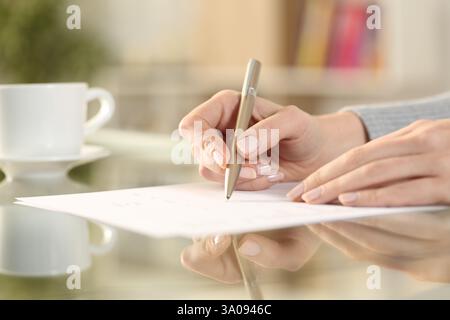 Primo piano di una donna che firma il contratto su una scrivania trasparente a casa Foto Stock