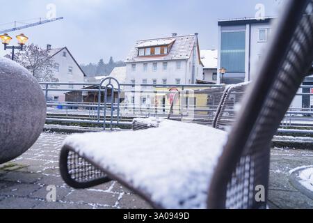 Atmosfera urbana invernale con panchina ricoperta di neve e edifici circostanti, Aidlingen, Boeblingen, Germania, Europa Foto Stock