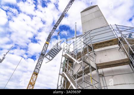 La gru da costruzione solleva la struttura delle scale accanto alla torre e all'impalcatura di fronte a un cielo nuvoloso, l'estensione della scala alla nuova torre del Calvo Foto Stock