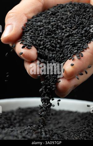 Mani che versano sesamo nero in primo piano Foto Stock