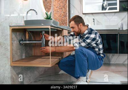 L'idraulico in uniforme blu è al lavoro in bagno. Foto Stock
