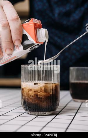 Versare il latte nel caffè ghiacciato in un bicchiere. Concetto di barista a domicilio, estetica minima da tavolo, preparazione delle bevande. Foto Stock