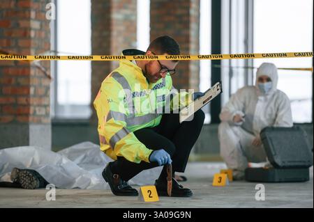 Indizio coltello. I detective stanno raccogliendo prove in una scena del crimine vicino al corpo morto. Gli specialisti forensi stanno facendo esperienza. Foto Stock
