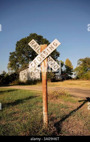 Segnaletica di attraversamento della ferrovia Rusty in un ambiente rurale con strade sterrate Foto Stock
