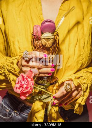 Donna che regge un bicchiere con i macaron Foto Stock