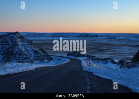 Sun setting over a winding road in the Badlands Foto Stock