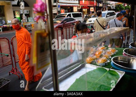 Bangkok, Thailandia. 18 febbraio 2025. Un monaco buddista passeggia davanti alle bancarelle di cibo di strada lungo la affollata Yaowarat Road, Chinatown, Bangkok, Thailandia Foto Stock